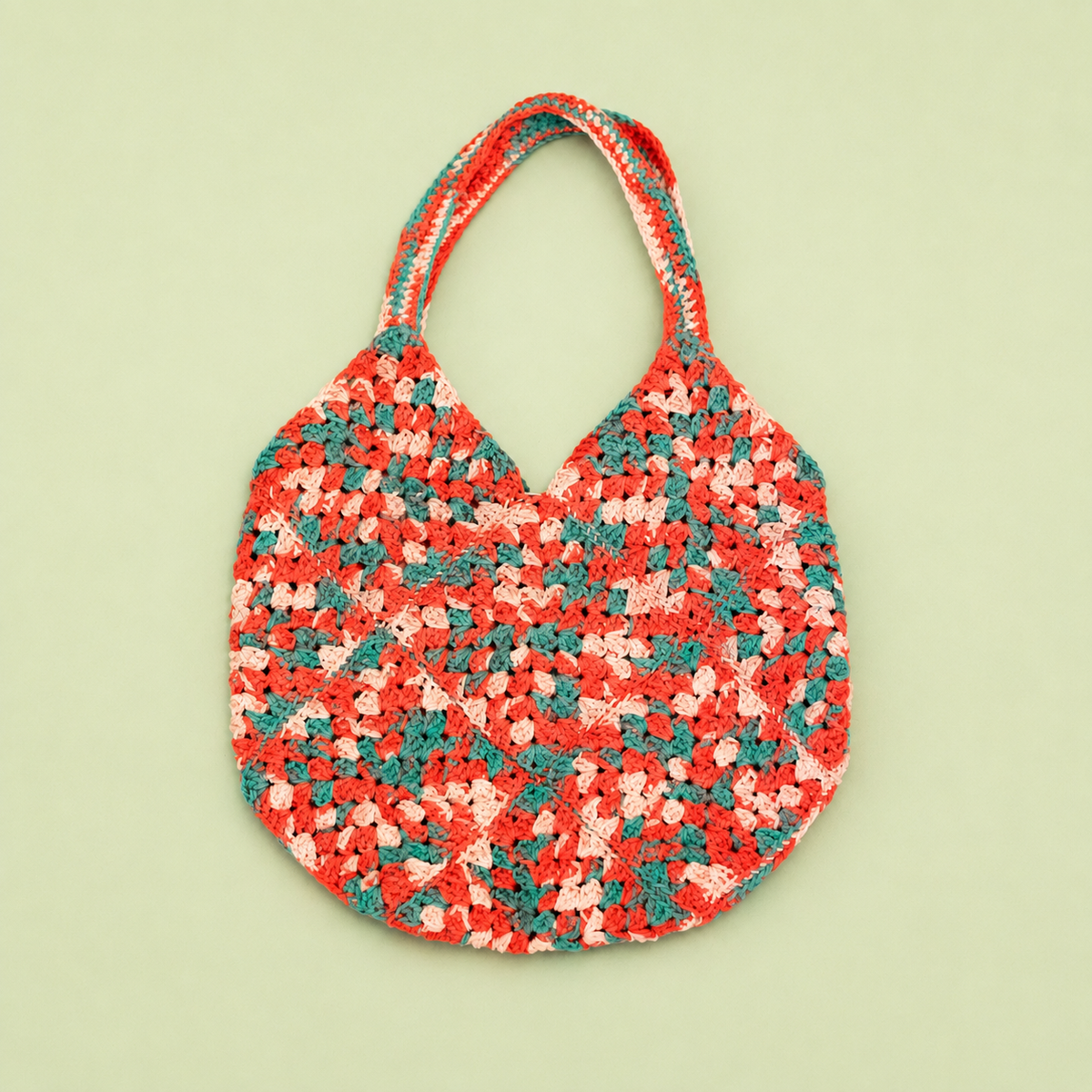 One of a kind handmade crochet bag in coral pink, blush and teal on a pale green background.