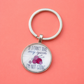 Silver keyring with round charm reading “If I can’t take my yarn I’m not going” with colourful balls of yarn on a coral pink background.