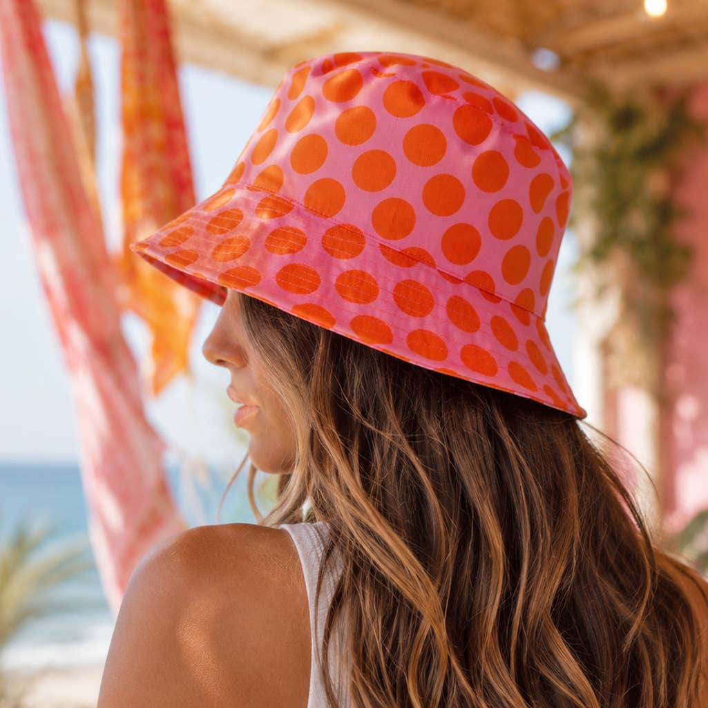 Person wearing a pink and orange polka dot bucket hat outdoors by the sea.