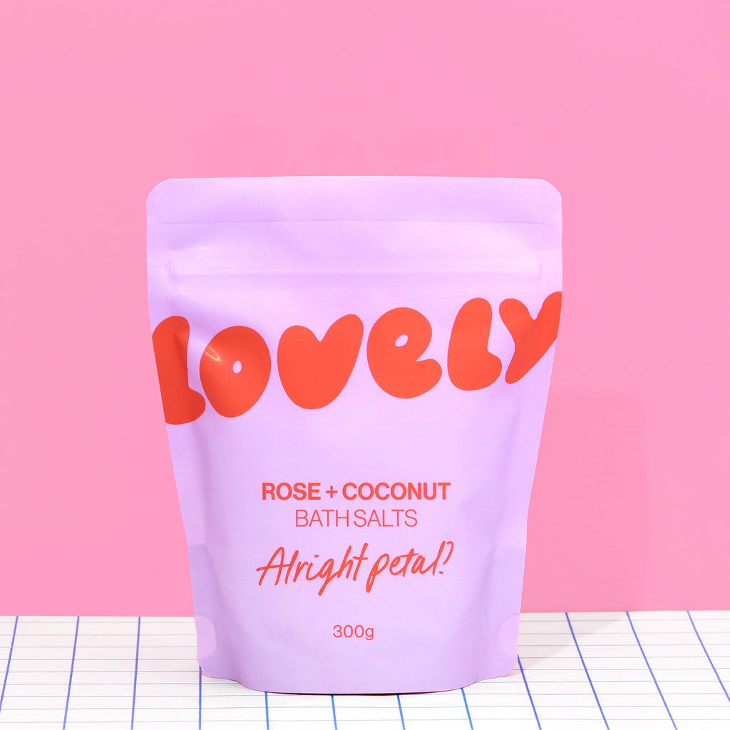 Rose and Coconut Bath Salts in lilac Alright Petal packaging against a bright pink background.