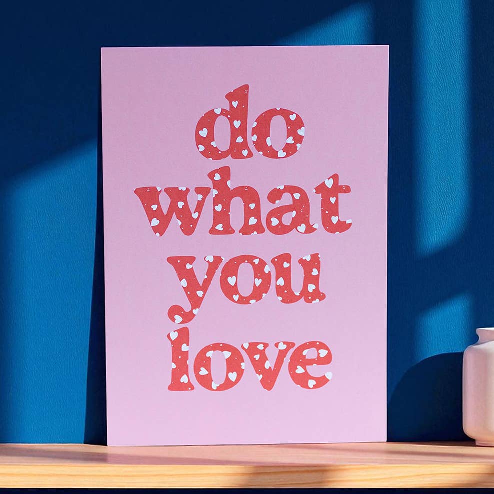 Joyful Do What You Love A5 print with coral heart patterned lettering on pink, styled against a rich blue background.
