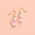 One of a kind gold plated drop earrings with pale pink glass heart beads, creamy pearl beads and soft green faceted beads on a peachy pink background.