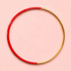 Red dip enamel stacking bangle with polished gold tone detailing on a pale pink background.