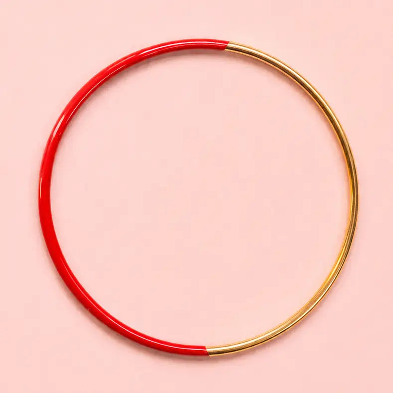 Red dip enamel stacking bangle with polished gold tone detailing on a pale pink background.
