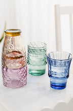 Multicoloured fish glasses partly stacked with green and blue tumblers filled with drinks and ice.
