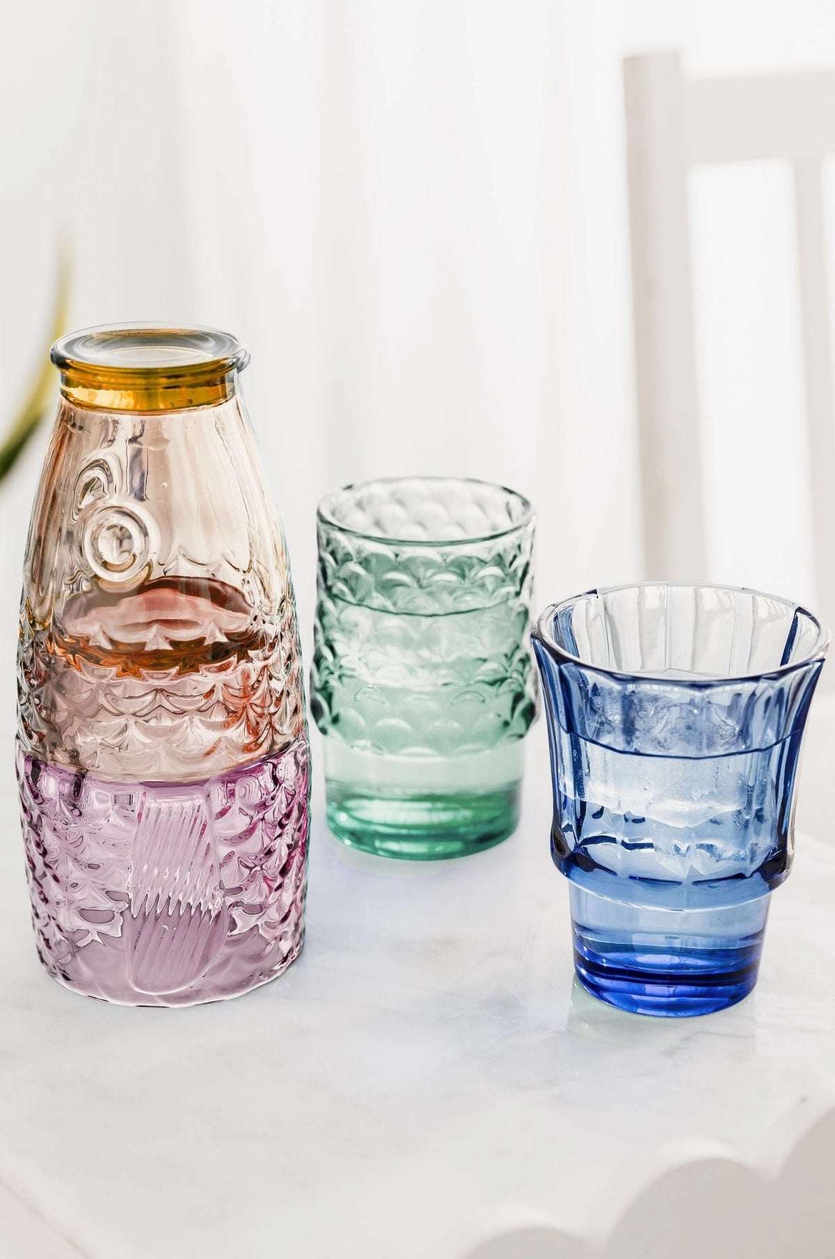 Multicoloured fish glasses partly stacked with green and blue tumblers filled with drinks and ice.