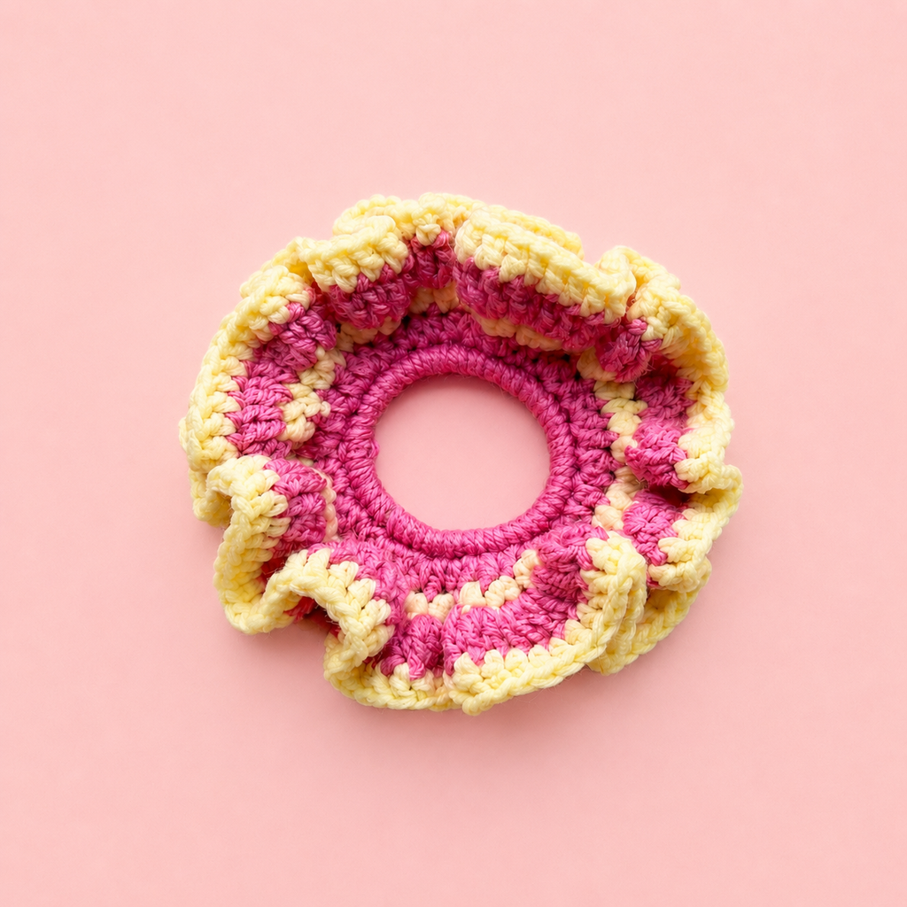 One of a kind Pink Lemonade crochet scrunchie handmade in bright pink and soft yellow on a pale pink background.