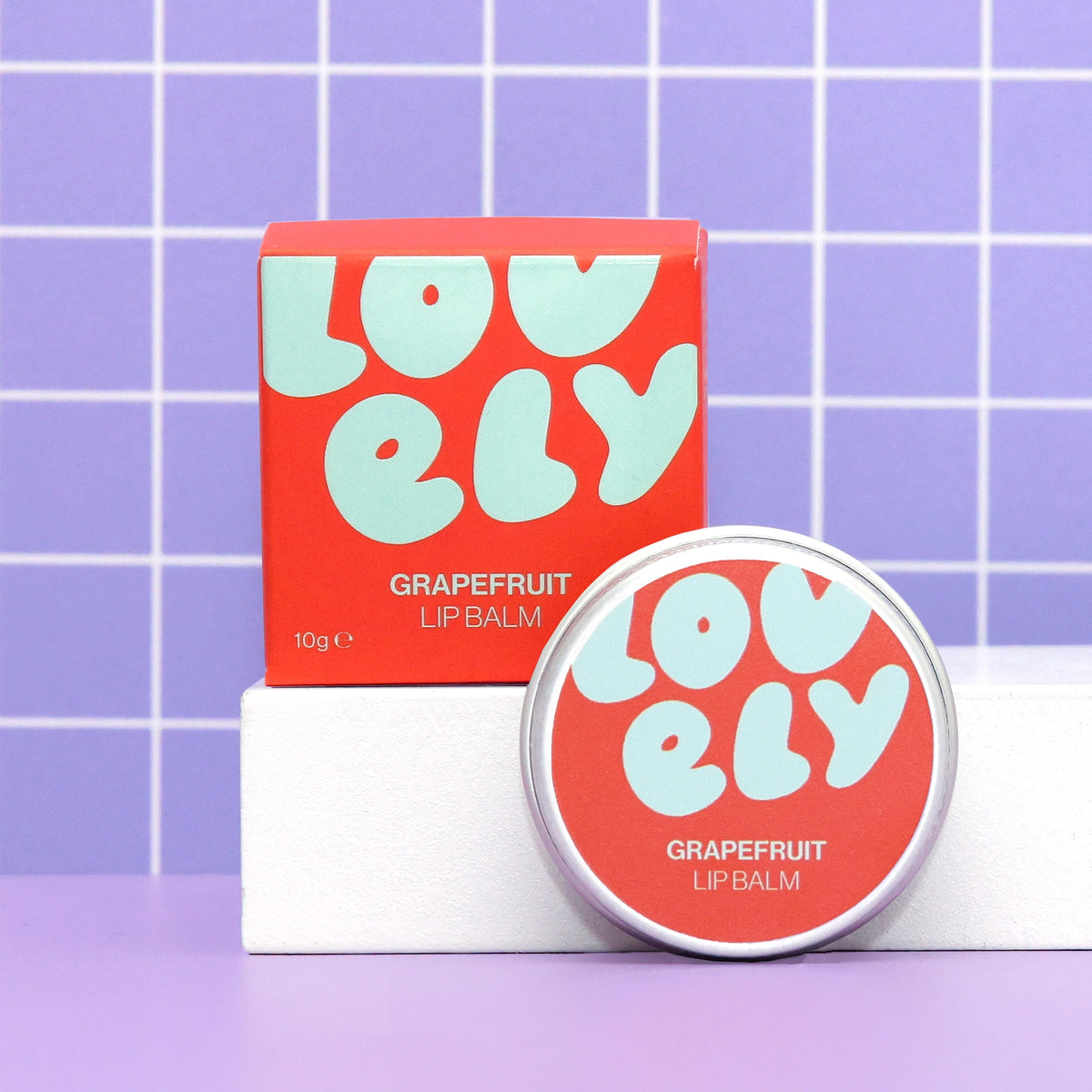 Grapefruit Lip Balm tin and colourful orange box displayed against a lilac tiled background.