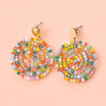 Pair of colourful beaded circular statement earrings with gold tone studs on a peach background.