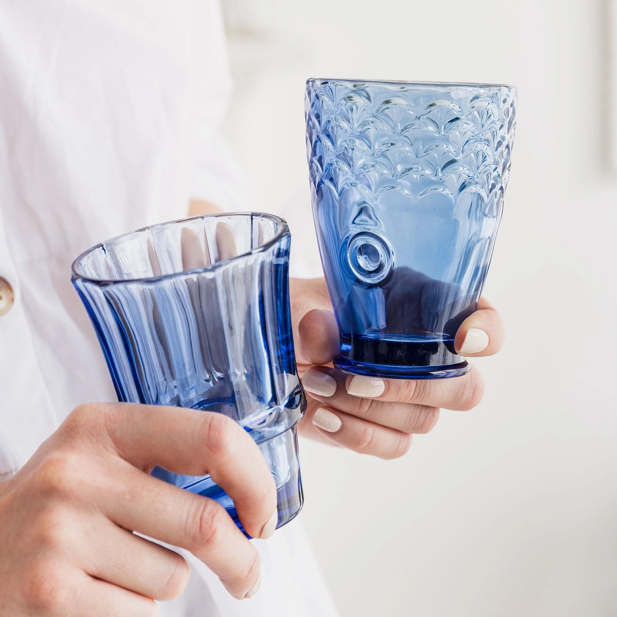 Two blue fish stacking tumblers held in hands showing their different shapes and textured details.