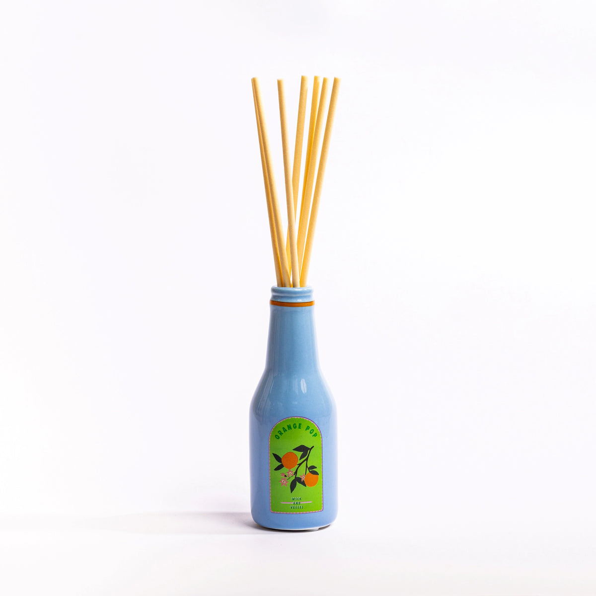 Blue Orange Pop reed diffuser bottle with natural reeds against a simple white background.
