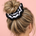 Black and white crochet scrunchie worn around a blonde messy bun, showing its oversized ruffled shape.