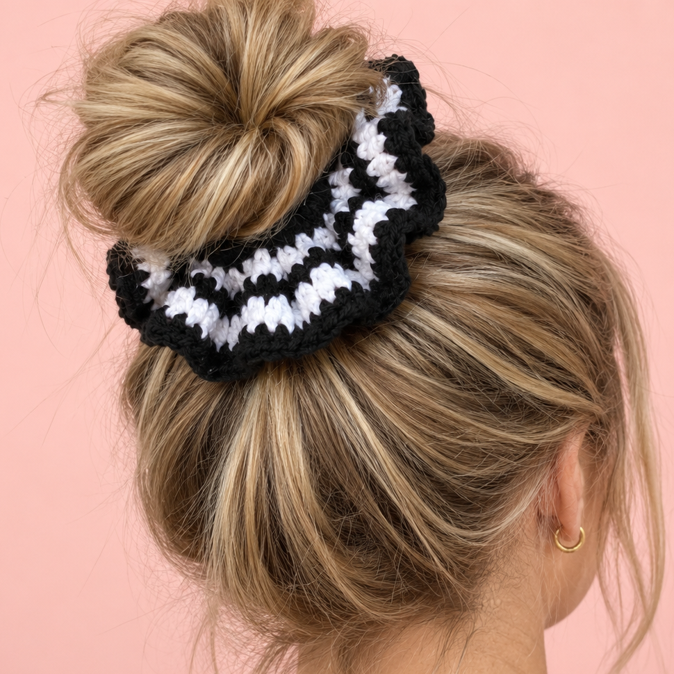 Black and white crochet scrunchie worn around a blonde messy bun, showing its oversized ruffled shape.