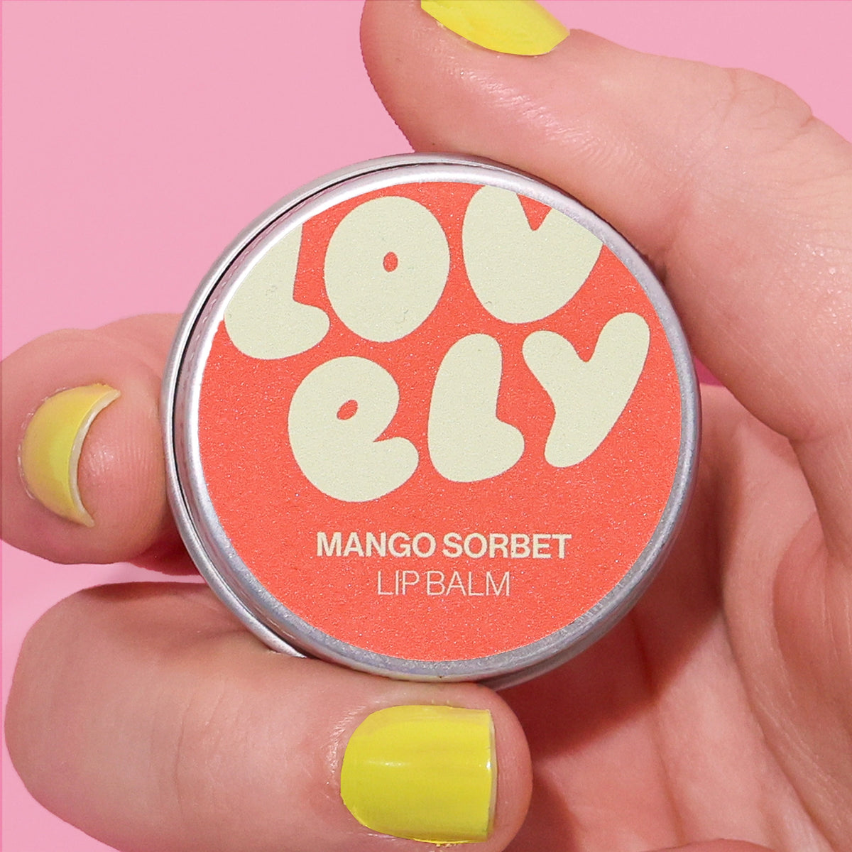 Mango Sorbet Lip Balm tin held in a hand against a pink background.