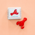 Red ceramic lobster token beside a gift box reading You Are My Lobster on a peach pink background.