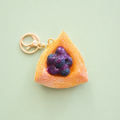 Blueberry Danish pastry bag charm keyring with golden pastry layers, glossy purple blueberries and gold clip on a pale green background.
