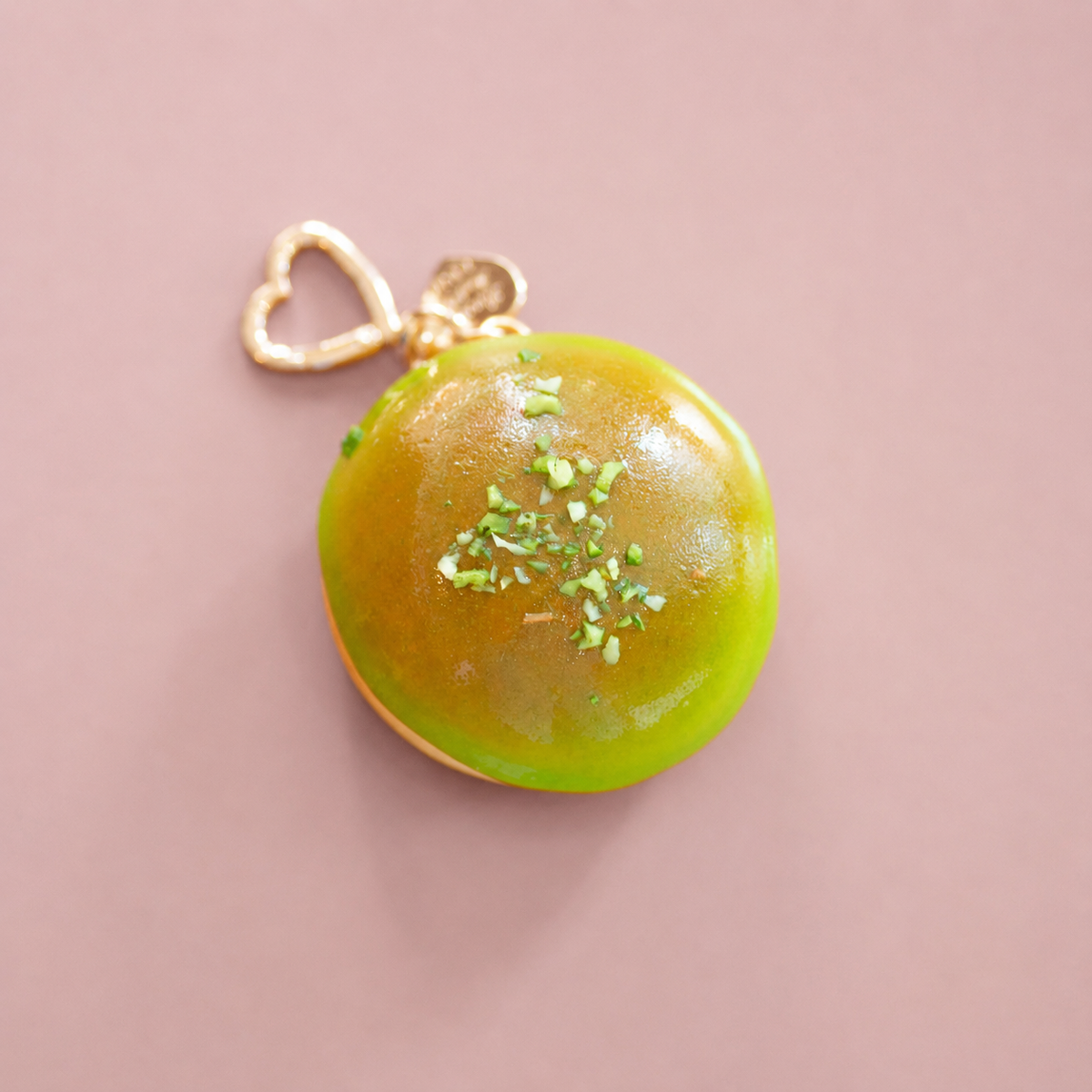Top view of green apple glaze doughnut bag charm with realistic icing and gold heart shaped clip.