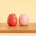 Red and soft pink ceramic tulip shaped salt and pepper shakers displayed on a wooden surface against a pale yellow background.
