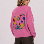 Back view of woman wearing pink jumper with large colourful floral AMOUR embroidery.