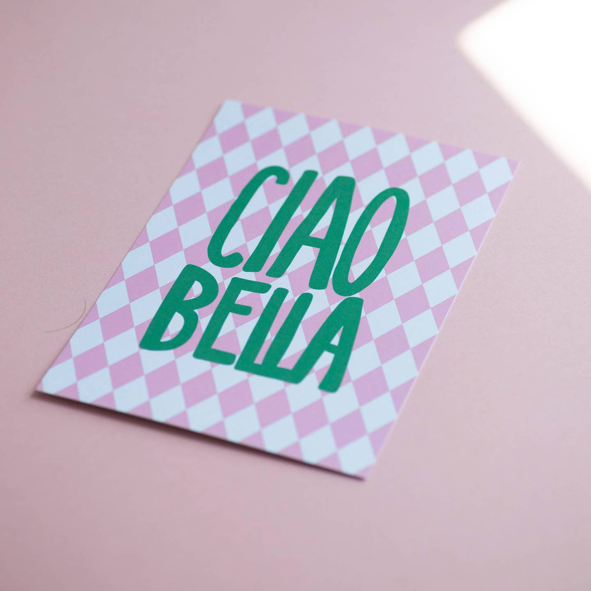 Colourful Ciao Bella A5 print with bold green lettering and pink diamond pattern, photographed on a soft pink background.