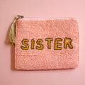 Pink beaded zip pouch with gold and yellow ‘SISTER’ lettering and metallic tassel zip pull.