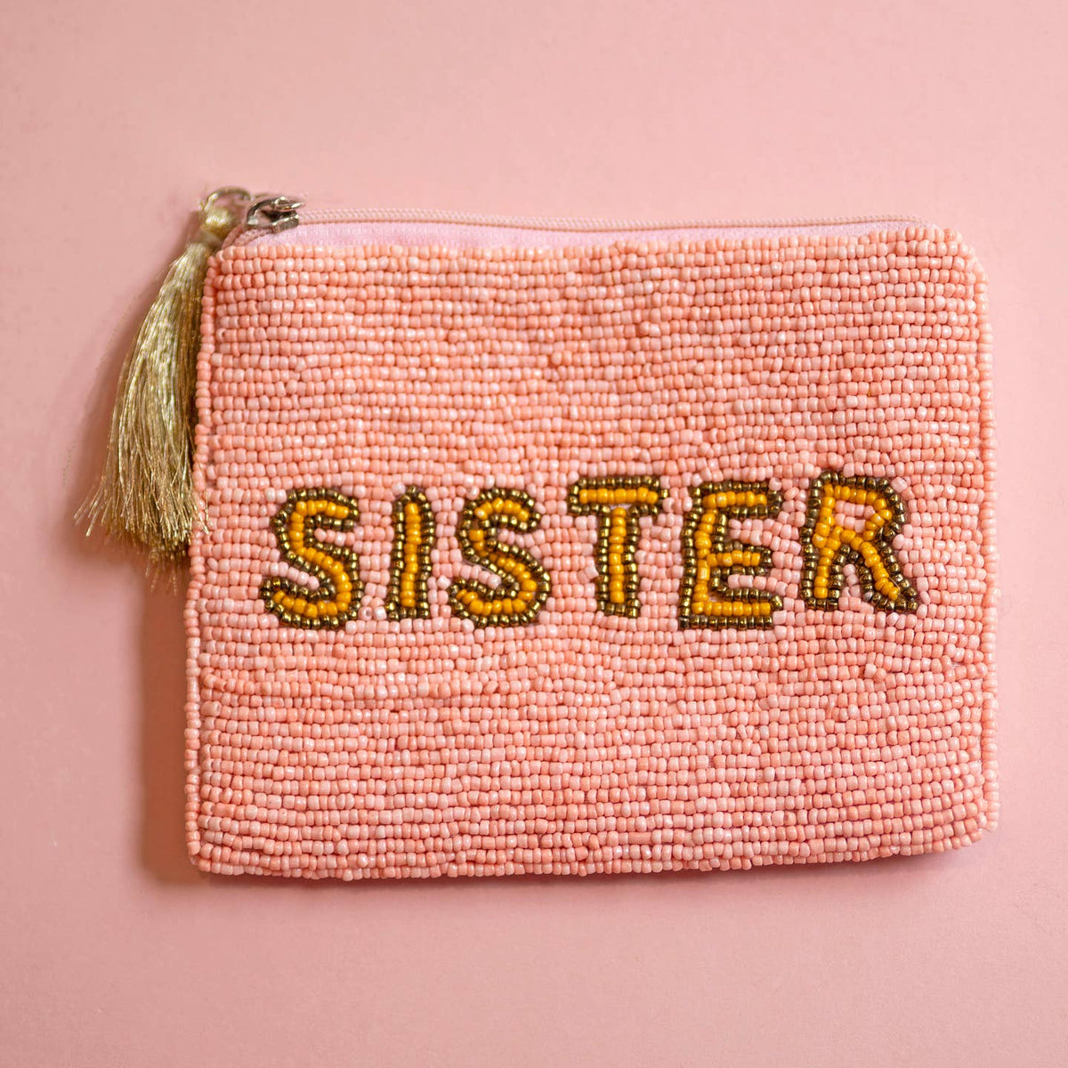 Pink beaded zip pouch with gold and yellow ‘SISTER’ lettering and metallic tassel zip pull.