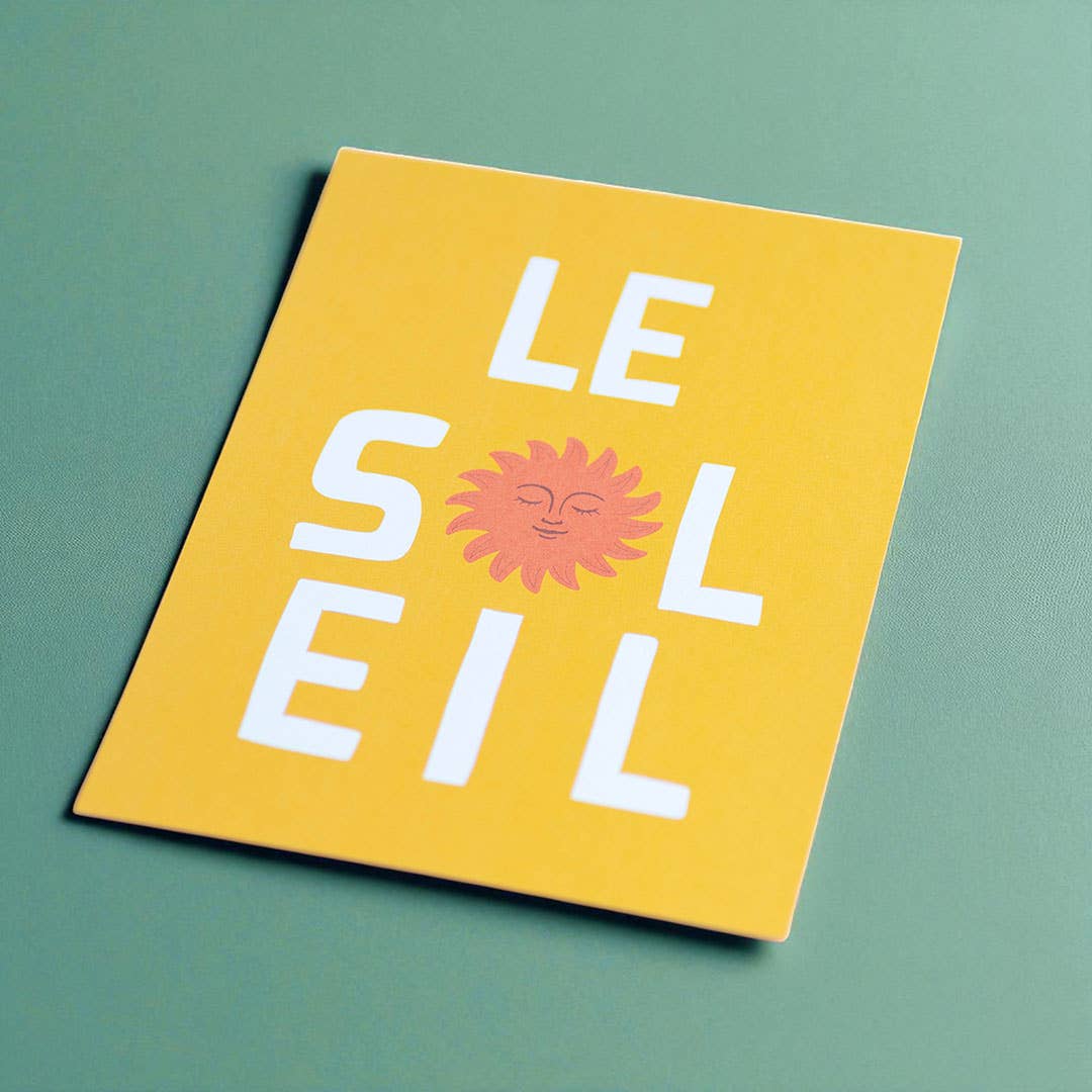 Cheerful yellow Le Soleil A5 art print with white lettering and a smiling coral sun displayed on a soft green background.