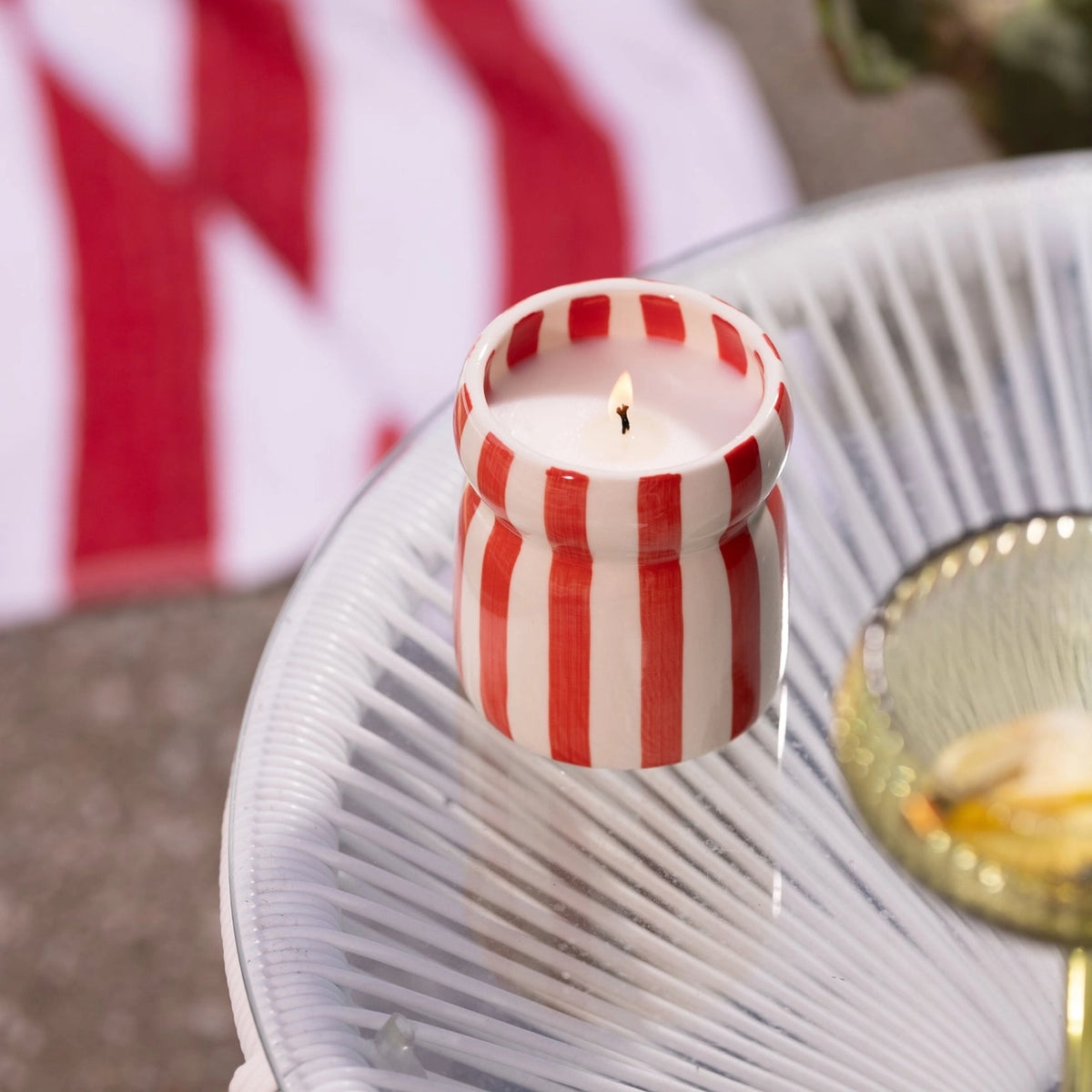 Lit Hibiscus Bay red and cream striped ceramic candle styled on an outdoor table.