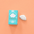 White ceramic Worry Cloud token with smiling face beside its illustrated gift box on a pink background. Available in two designs, selected at random.