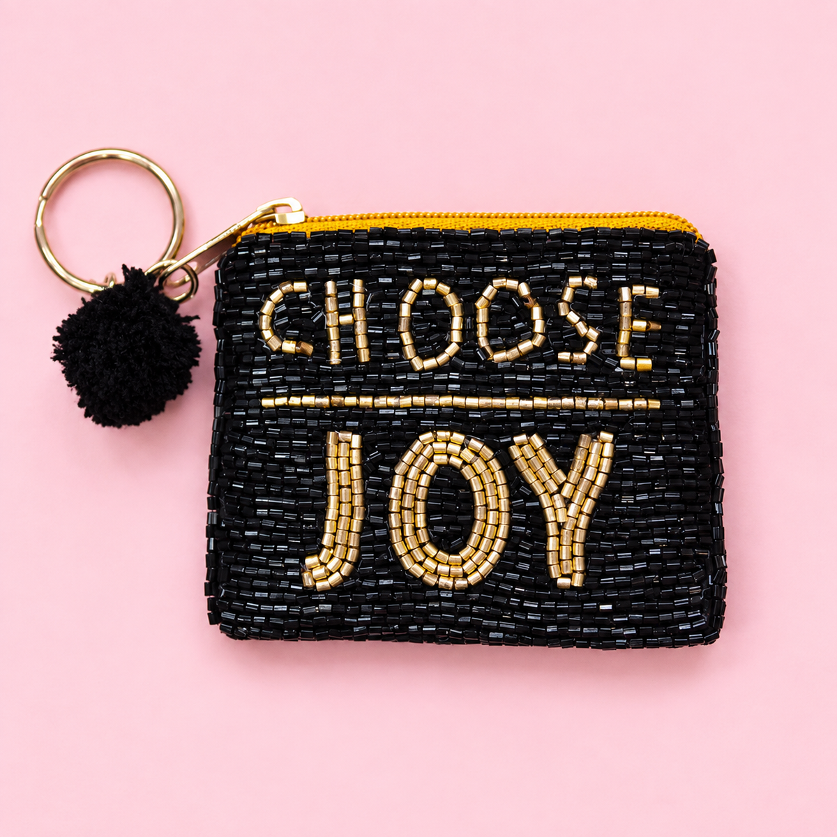 Black beaded mini coin purse keyring with gold Choose Joy lettering, black pom pom and gold tone keyring on a pink background.