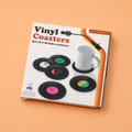 Boxed set of six black vinyl record drinks coasters with colourful retro style centre labels on an orange background.