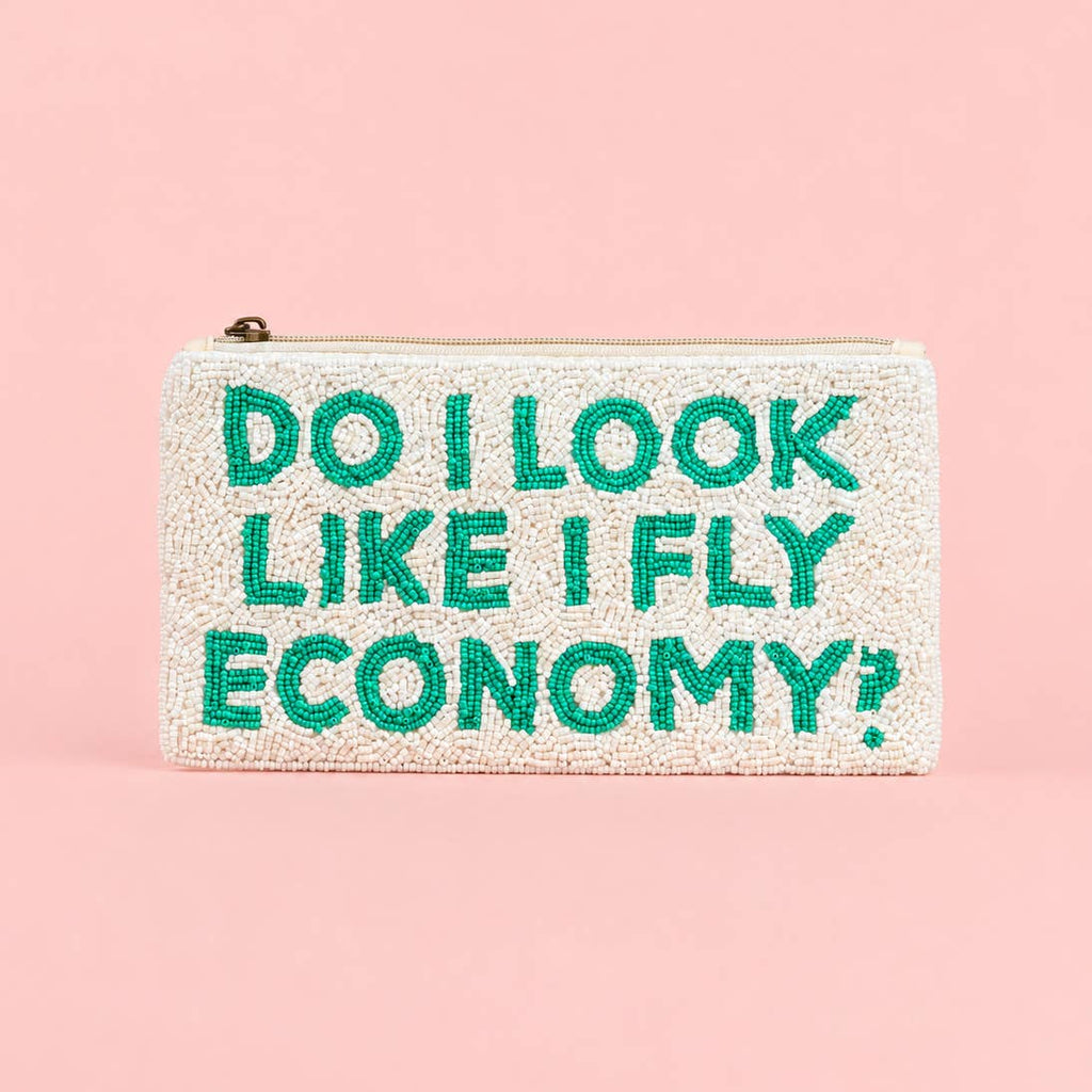 Cream beaded zip travel wallet with turquoise ‘Do I Look Like I Fly Economy?’ slogan on a pink background.