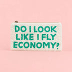 Cream beaded zip travel wallet with turquoise ‘Do I Look Like I Fly Economy?’ slogan on a pink background.