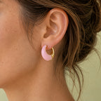 Pale pink and gold-tone enamel huggie hoop earring styled on the ear, showing its chunky curved shape.