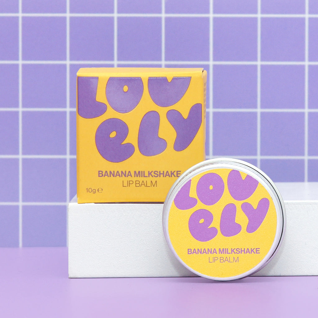 Banana Milkshake Lip Balm 10g tin and colourful yellow and purple box on a lilac background.