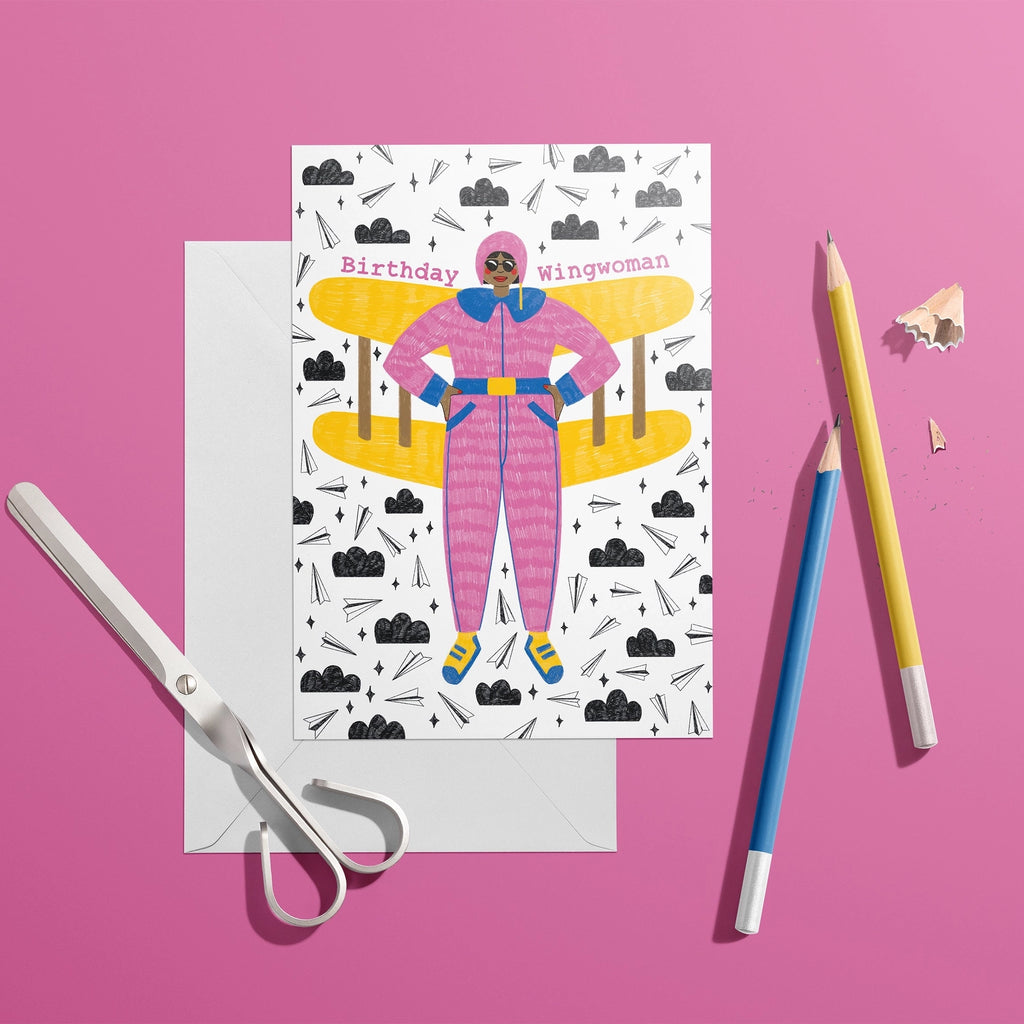 Colourful Birthday Wingwoman card featuring a woman in a pink flying suit with yellow plane wings, styled on a bright pink background.