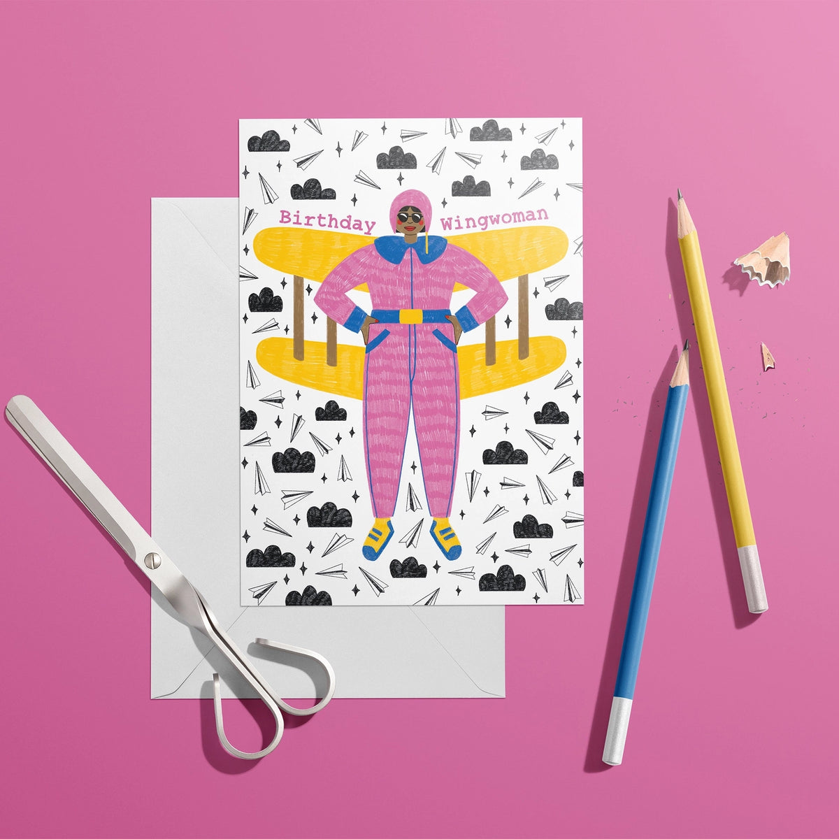 Colourful Birthday Wingwoman card featuring a woman in a pink flying suit with yellow plane wings, styled on a bright pink background.