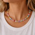 Woman wearing a colourful pastel crystal cube bead necklace with a white top.