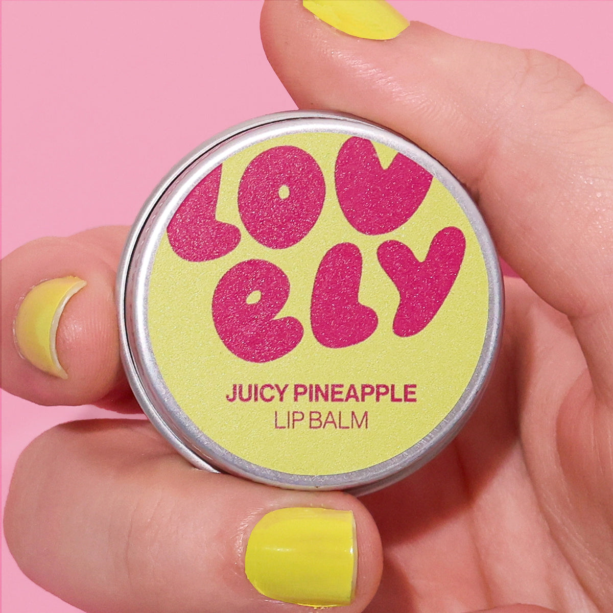 Grapefruit Lip Balm tin held in a hand against a pink background.
