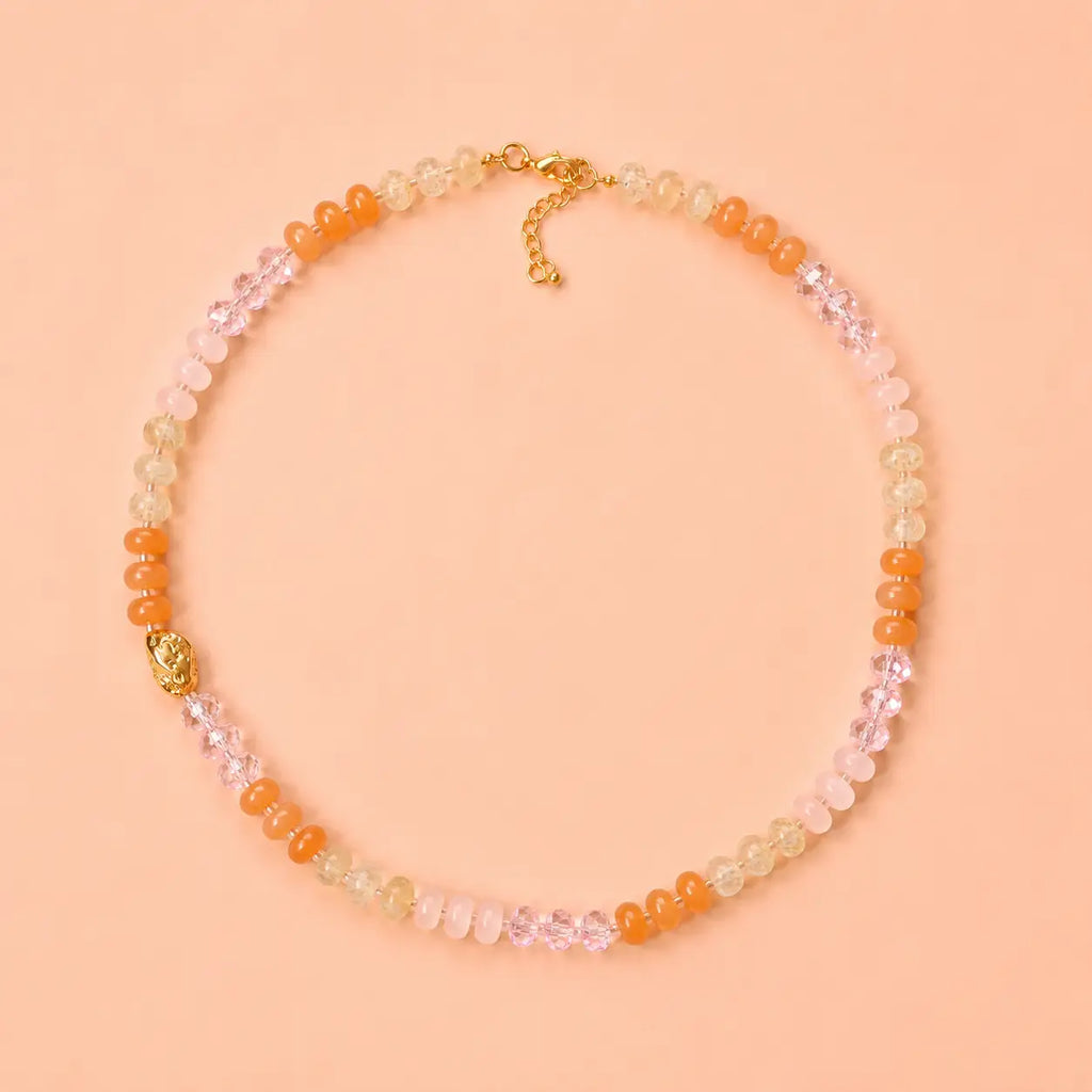 Sunrise natural stone bead necklace with peach, blush pink, honey and crystal accent beads on a peach background.