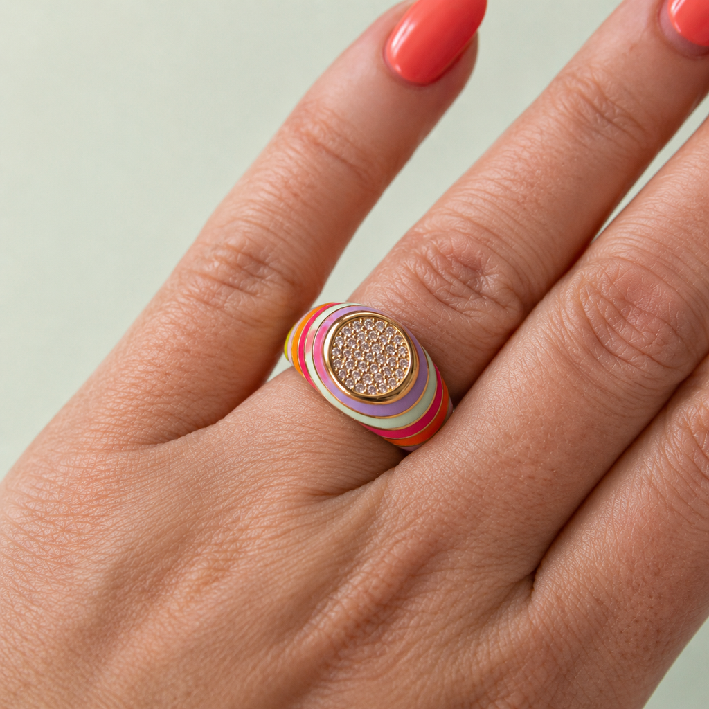 Multicolour enamel gold tone signet ring with sparkling crystal centre worn on a hand.