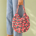 Woman in blue jeans holding a handmade crochet shoulder bag in coral pink, blush and teal.