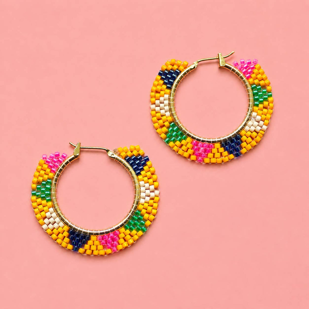 Yellow beaded hoop earrings with pink, green, navy and white glass bead details on a pink background.
