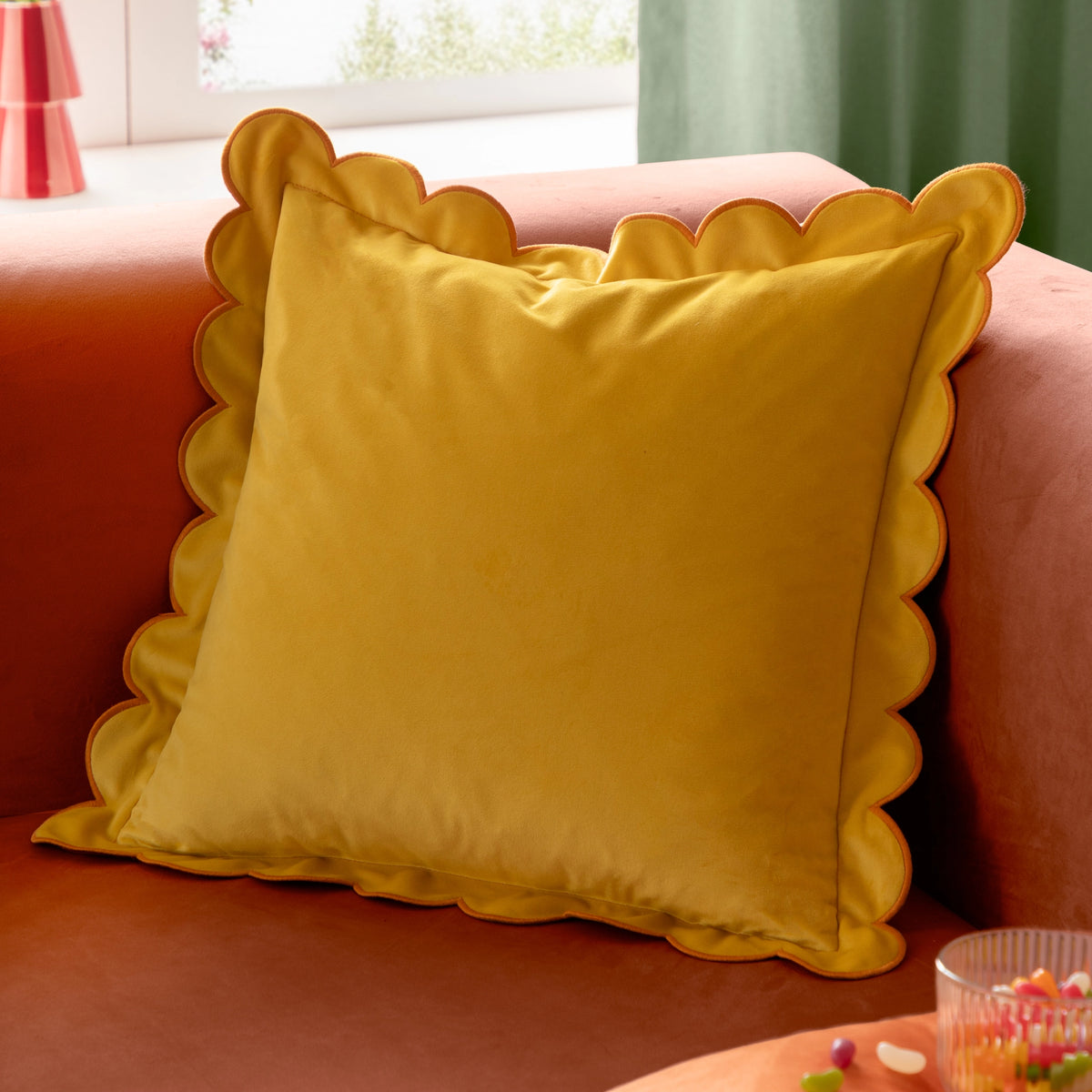 Yellow velvet cushion with scalloped edging and contrasting orange trim styled on an orange sofa.
