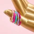 Colourful pink, turquoise, lilac and pale pink enamel CZ rings displayed together on a gold hand against a pink background.