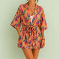 Colourful peach kimono robe with a vibrant tropical leaf print, wide sleeves and matching tie belt, styled for a joyful relaxed look.