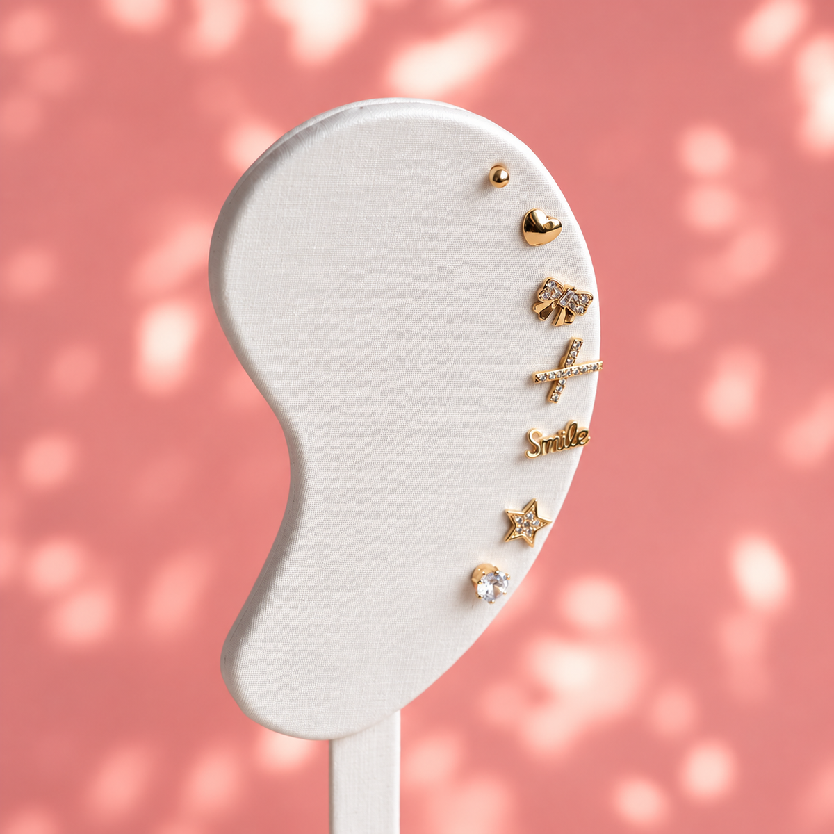 Seven different gold plated stud earrings from the Week of Earrings set displayed on a white earring stand.