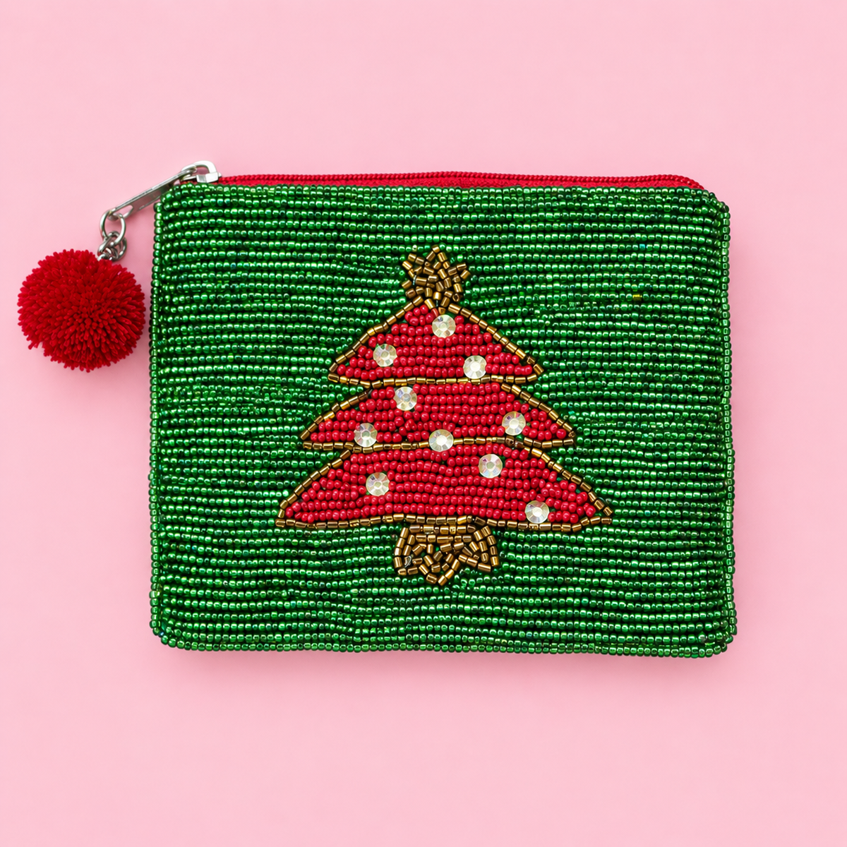 Green beaded zip pouch with red Christmas tree design, sparkling gems and red pom pom zip pull on a pink background.