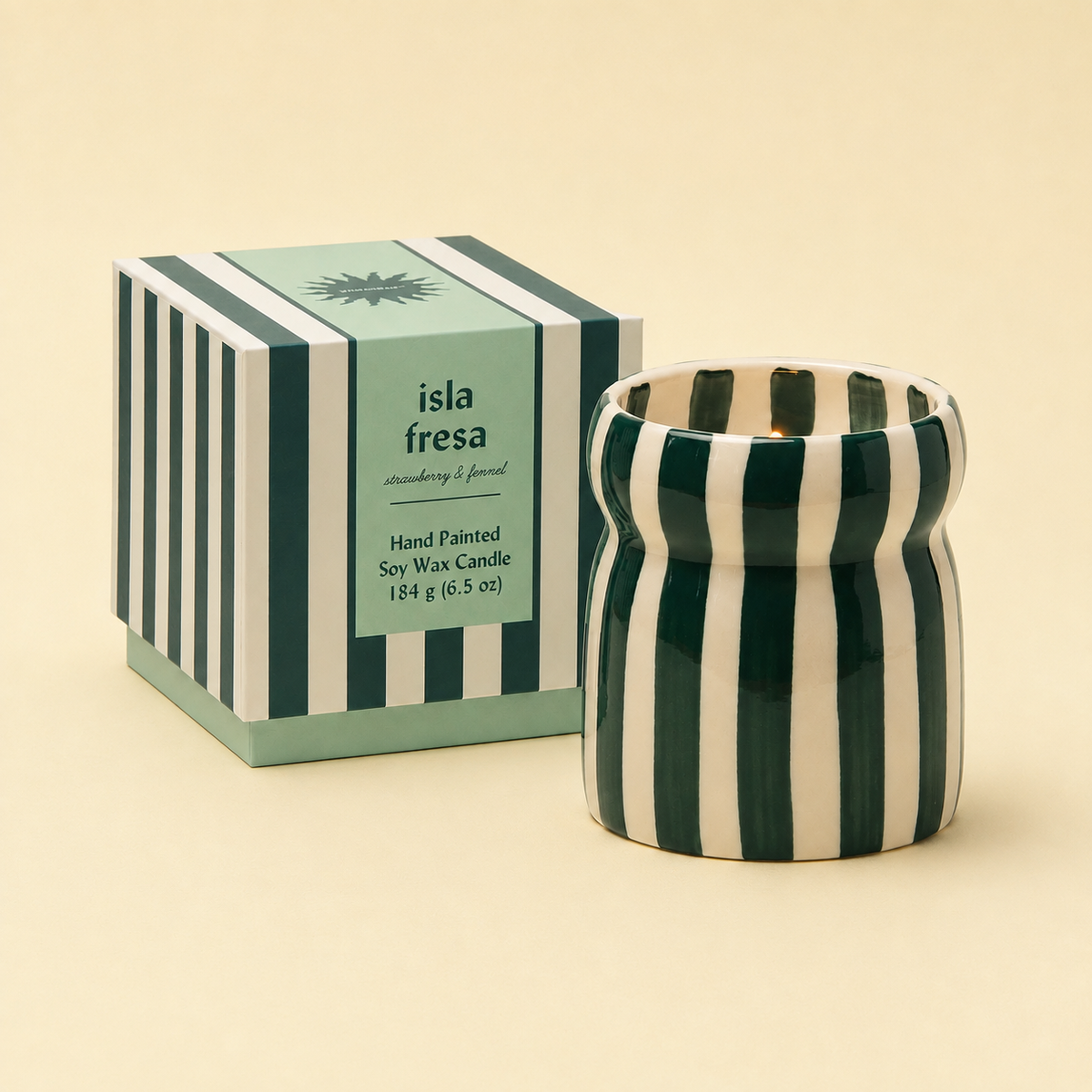 Isla Fresa soy wax candle in a green and cream striped ceramic vessel beside its matching presentation box.