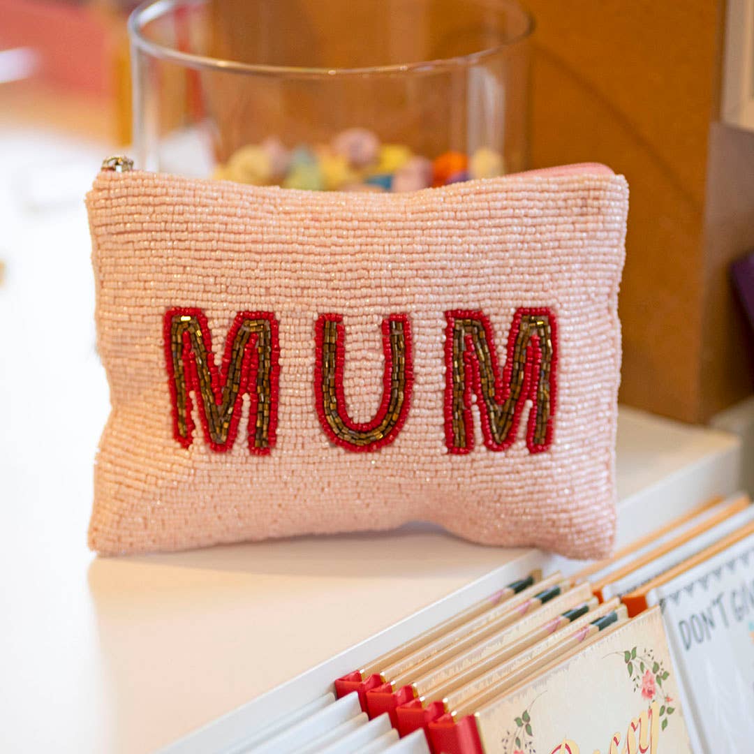 Pink beaded ‘MUM’ pouch with red and gold lettering displayed on a shelf.